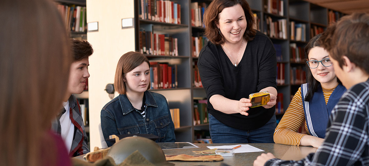 A group of people sitting around a table with their teacher, looking at Discovery Box artifacts.