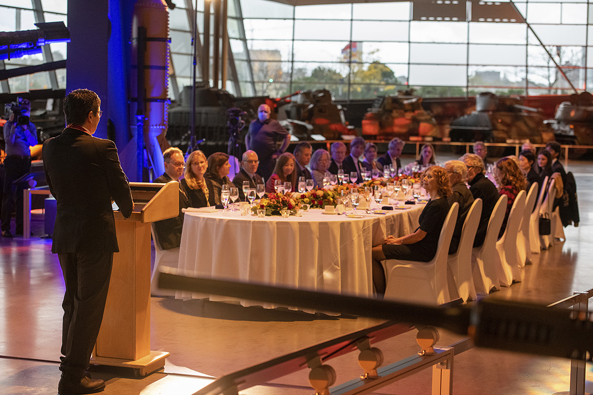 A man standing at a table in front of a crowd of people in Ottawa.