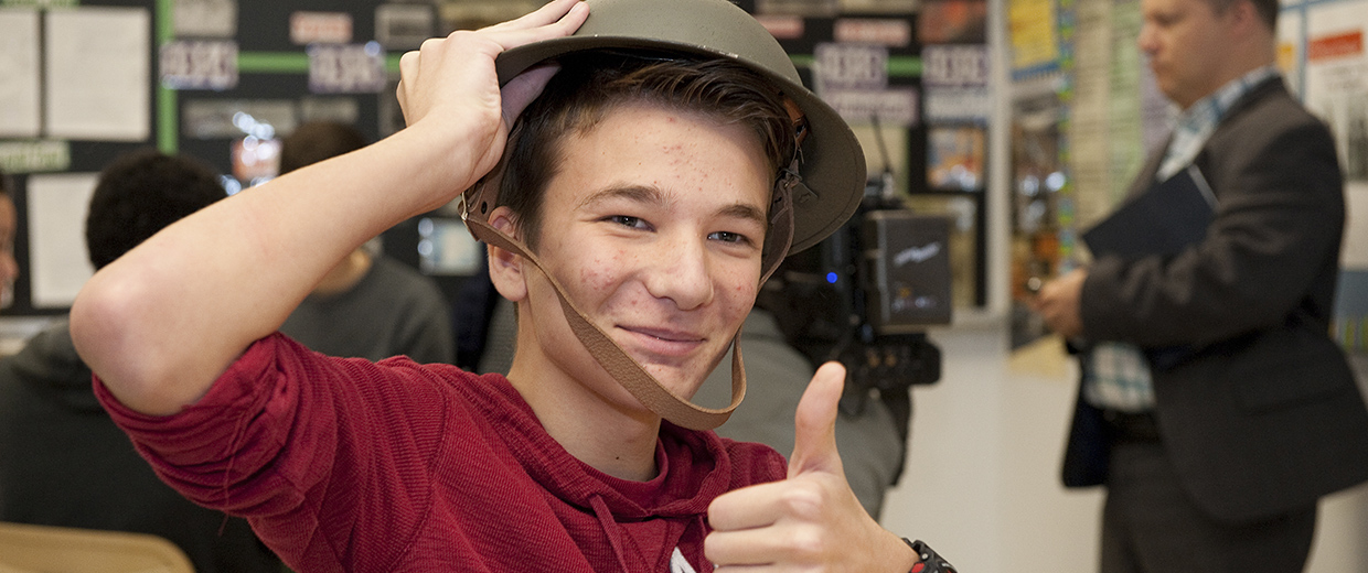 A boy wearing a hat and giving a thumbs up in Ottawa near the Canadian War Museum.