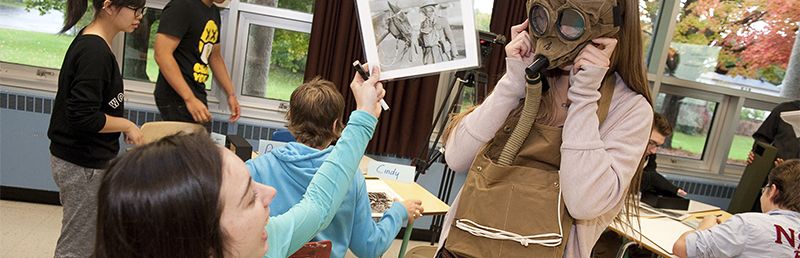 A group of people in a classroom a learning about war gas masks.