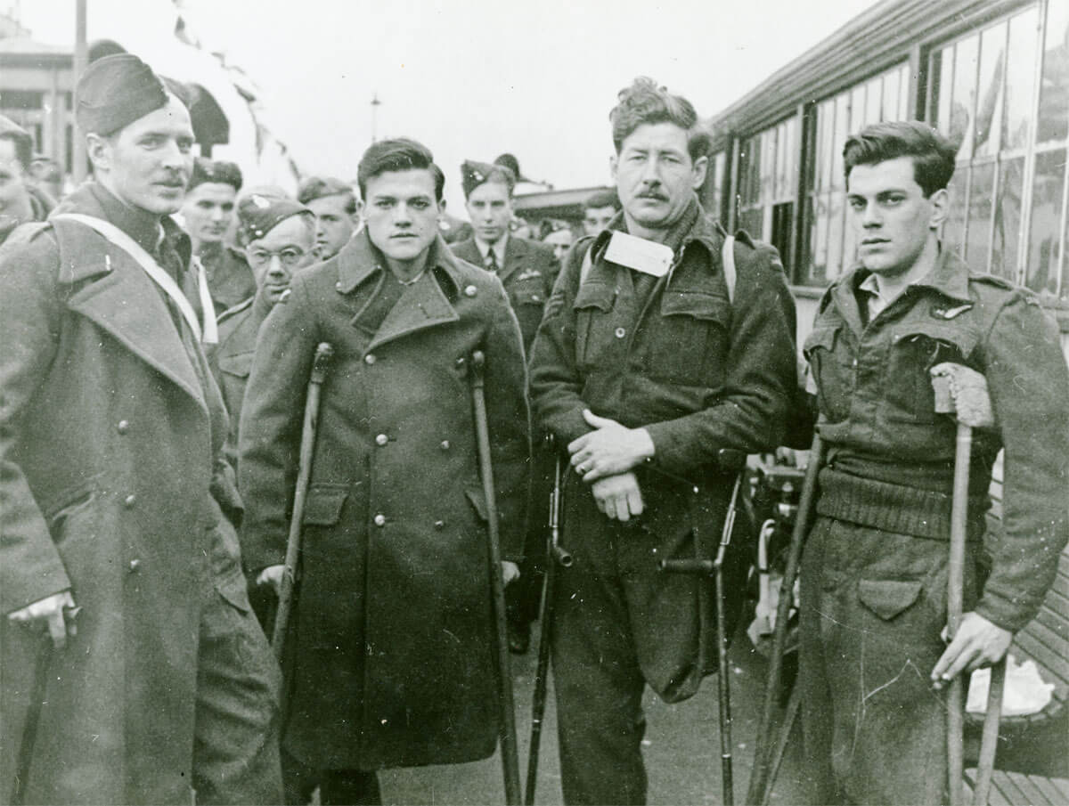 A group of soldiers with crutches standing next to a train.