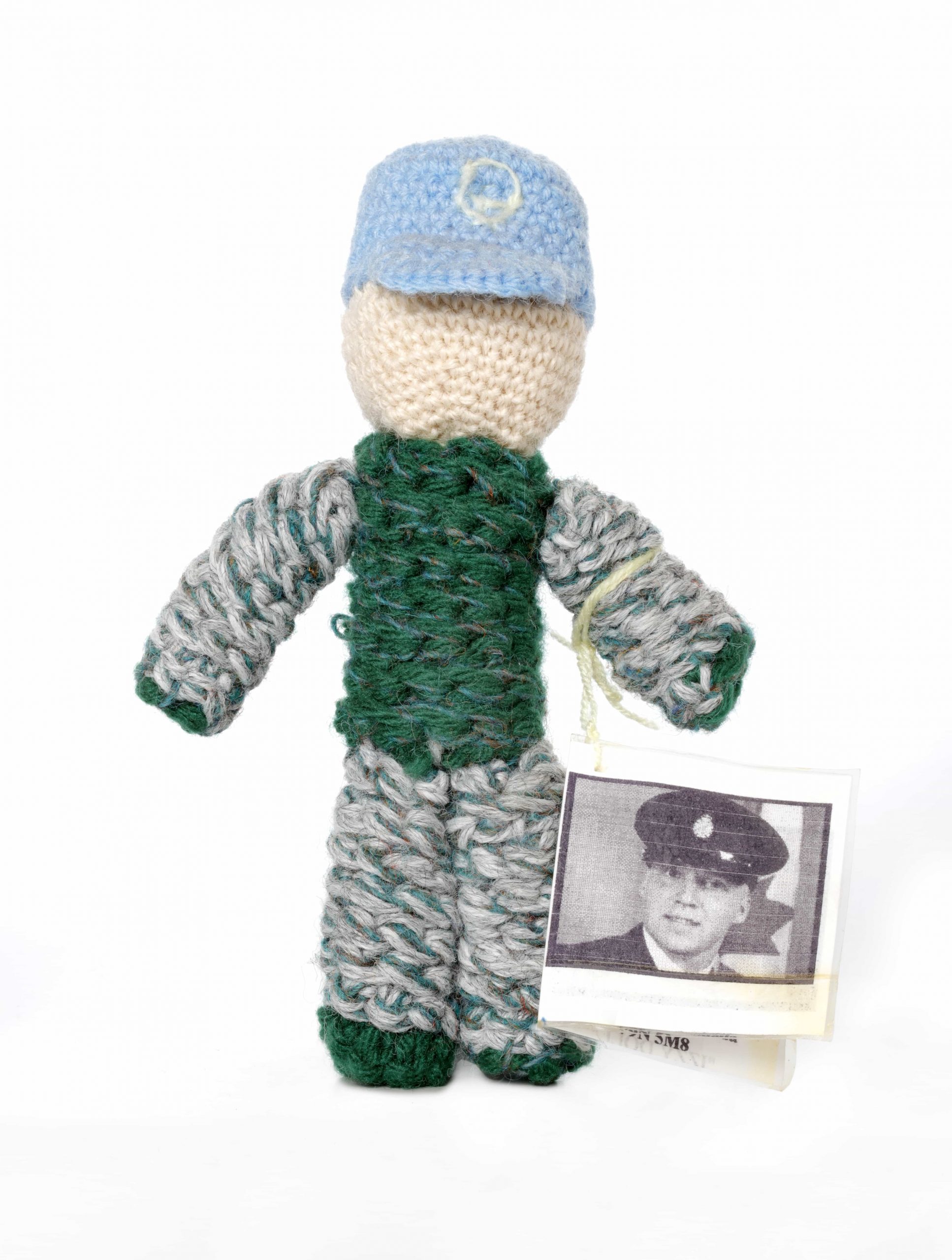 A knitted Izzy doll with a picture of a soldier.