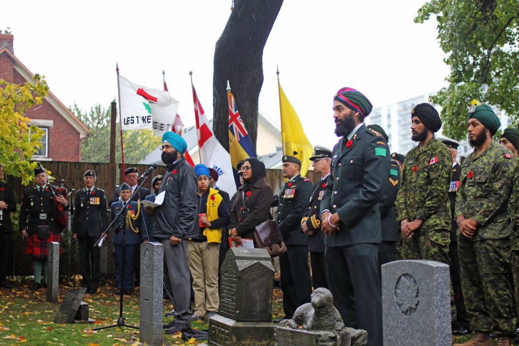 A group of people standing in front of a grave with flags in Ottawa.