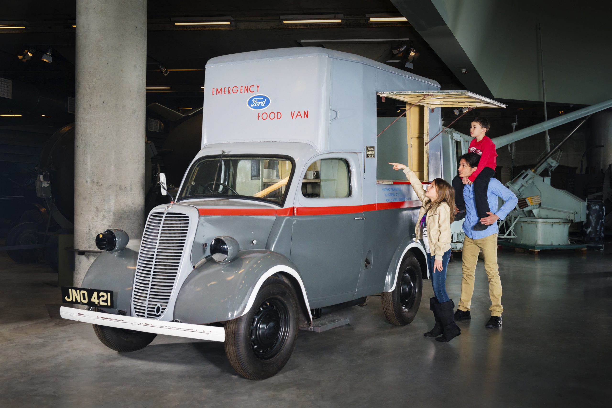 A family is standing next to a vintage truck in a museum.