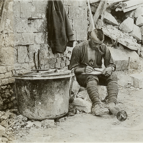 Soldier writing a letter and seated in rubble.