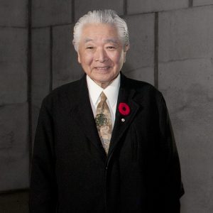 A man in a suit standing in front of a concrete wall.